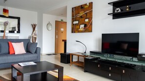 Un salon moderne avec un canapé gris, une table basse, un téléviseur à écran plat, une table basse en verre et un meuble de rangement noir pour appareils multimédias.