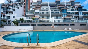 Een modern appartementencomplex met een zwembad, balkons en uitzicht op zee.