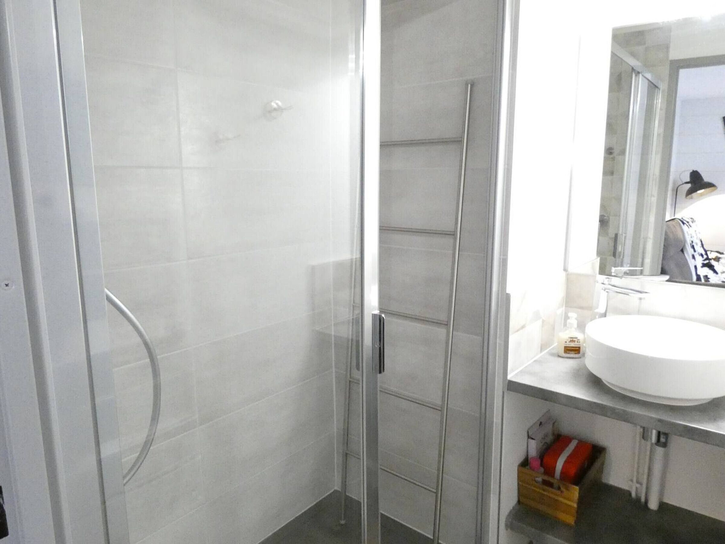 A modern bathroom with a glass shower enclosure, a white sink, and a mirror above it.