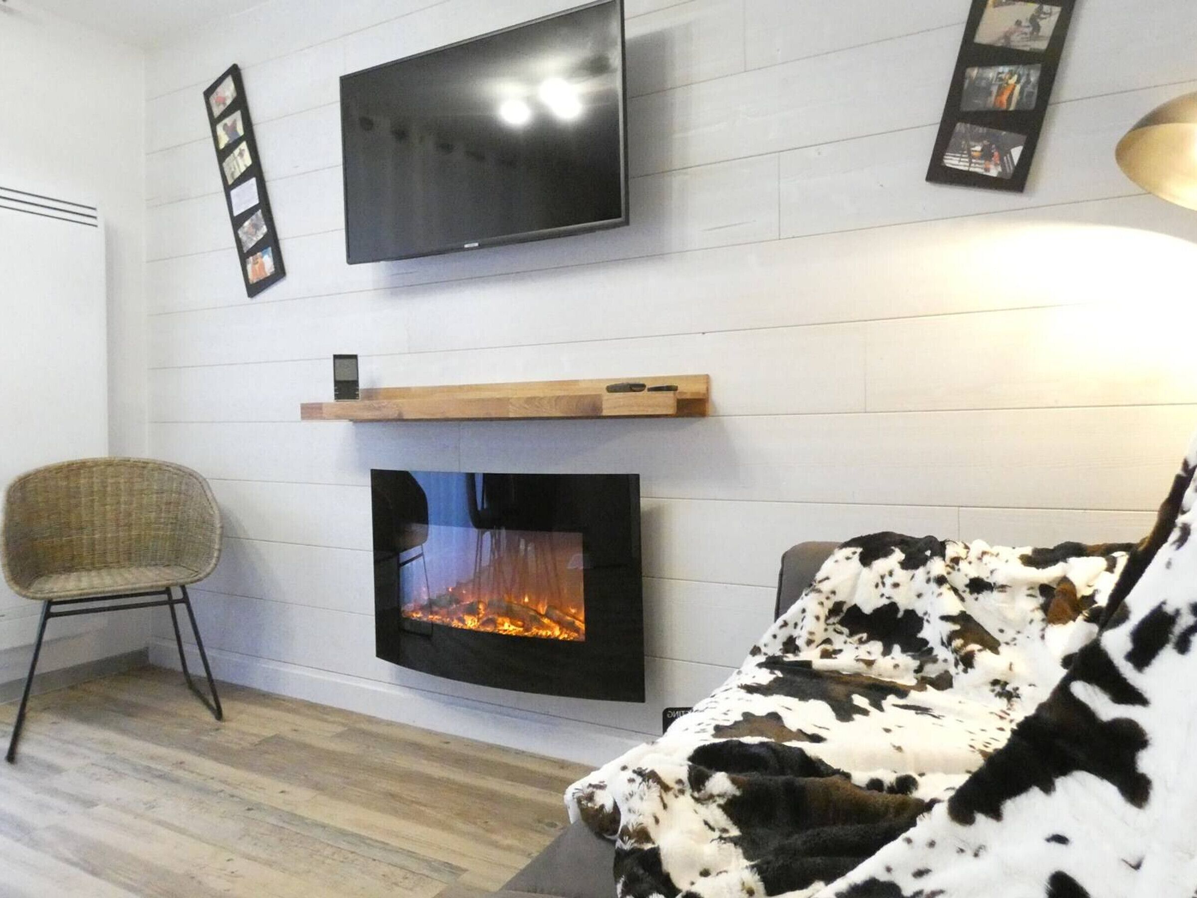 A modern living room with a flat-screen TV, a fireplace, a framed photo collage, and a comfortable sofa.