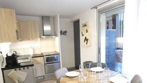 A compact kitchen with modern appliances, a dining area with a round table set for four, and a view of the outside through a sliding door. - Charming 2-Bedroom Apt with Balcony, Mountain Views, WiFi, Parking & Baby Gear in St Lary Soulan (Vignec)