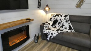 A modern living room with a fireplace, a sofa, a TV mounted on the wall, and a lamp. - Charming 2-Bedroom Apt with Balcony, Mountain Views, WiFi, Parking & Baby Gear in St Lary Soulan (Vignec)
