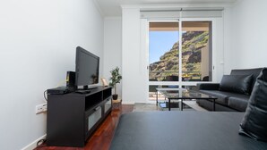 Un salon moderne avec un téléviseur à écran plat, un meuble de rangement noir, un canapé noir et une table basse en verre.