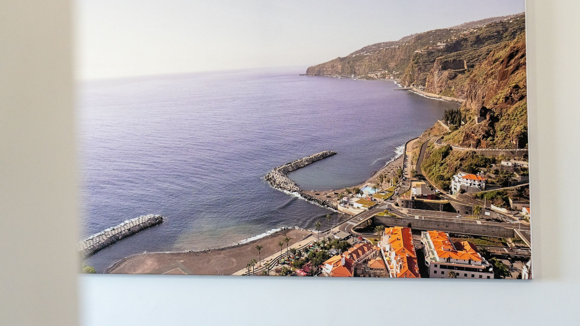 A coastal town with a rocky shoreline, a pier, and buildings with red roofs.