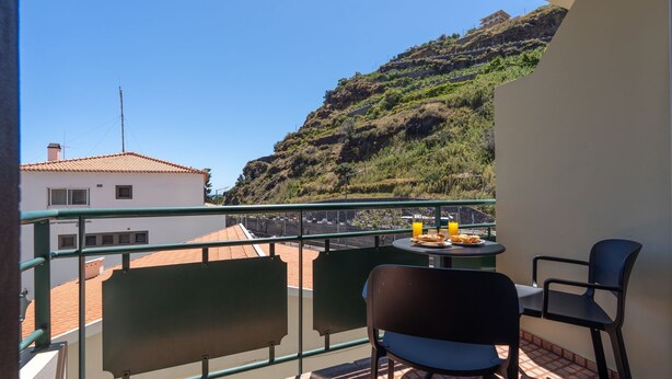 Un balcon avec une table, deux chaises et une vue sur une colline.