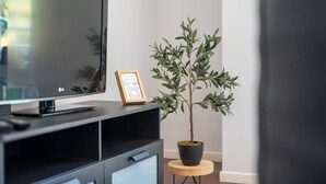 Un salon moderne avec un téléviseur à écran plat, un code QR encadré et un olivier en pot.