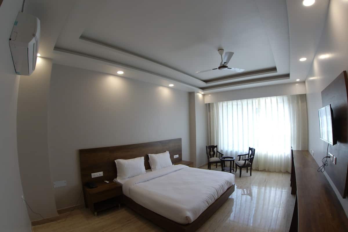 A hotel room with a large bed, a desk, a chair, a ceiling fan, and a TV mounted on the wall.