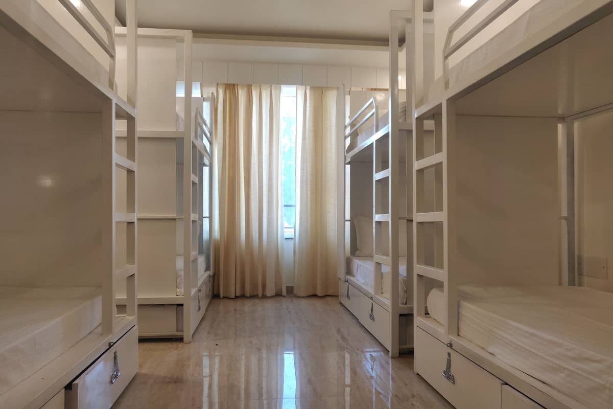 A room with bunk beds, a window with curtains, and a wooden floor.