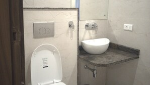 A bathroom with a toilet, sink, mirror, and a trash can. - Backpacker Panda Rishikesh (Narendranagar)