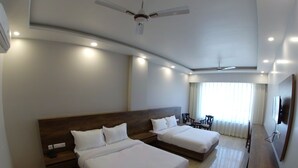 A hotel room with two beds, a ceiling fan, recessed lighting, a TV, and a large window with curtains. - Backpacker Panda Rishikesh (Narendranagar)