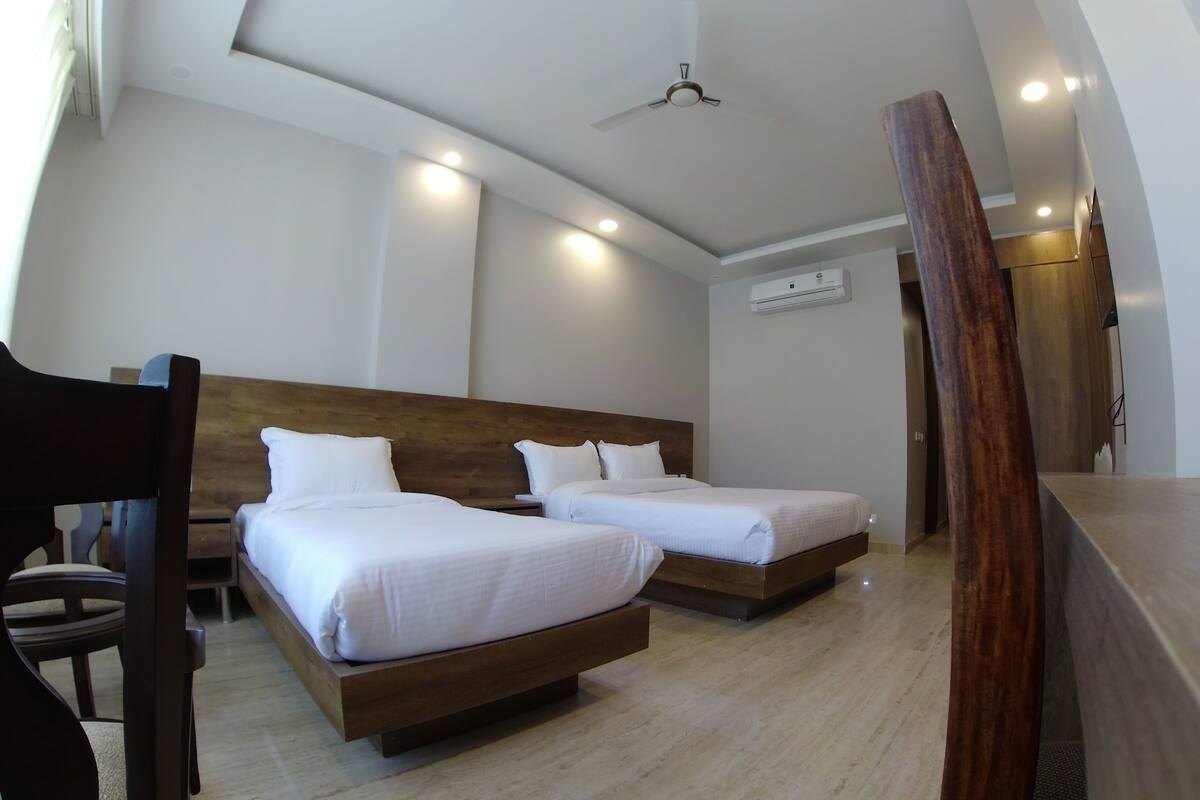 A hotel room with two beds, a wooden headboard, a ceiling fan, and an air conditioning unit.