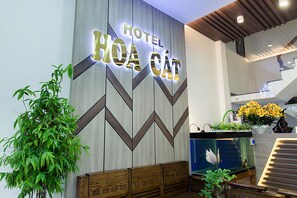 A hotel reception area with a modern design, featuring a large illuminated sign, a reception desk, and a staircase. - Hoa Cat Hotel (Quy Nhon Nam)