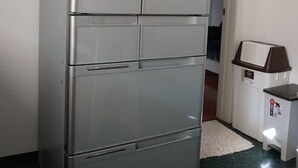 Een koelkast van roestvrij staal met een vriesvak bovenin en een hoofdcompartiment eronder, in een keuken met een marmeren aanrecht en een witte deur op de achtergrond.