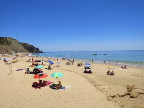 A beach with people sunbathing and swimming, umbrellas, and boats in the water. - Cristaluz in central location, 5 mins walk to shops, restaurants and the beach ! (Praia da Luz)