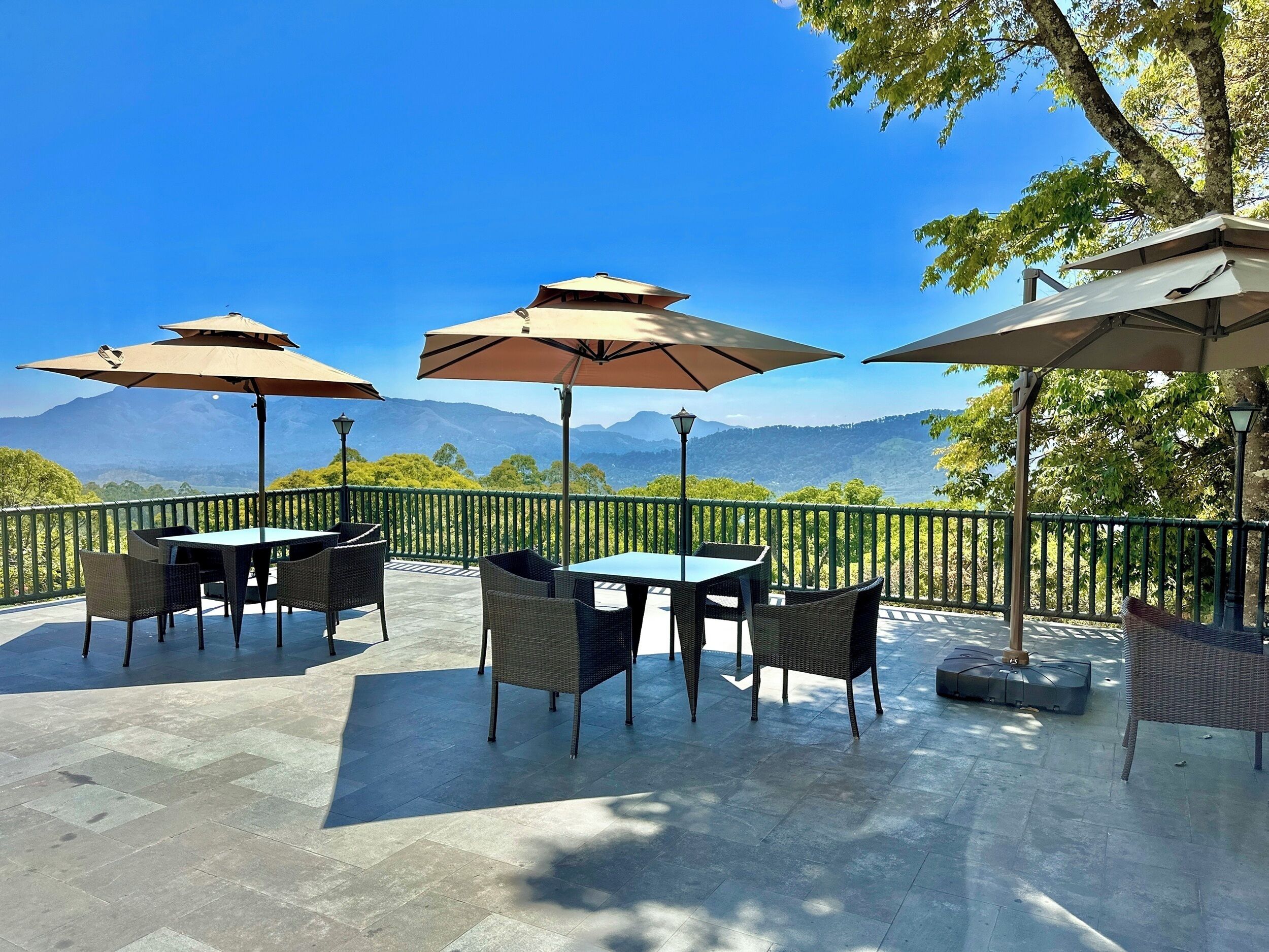 Un patio al aire libre con mesas y sillas, sombrillas y vistas a las montañas.