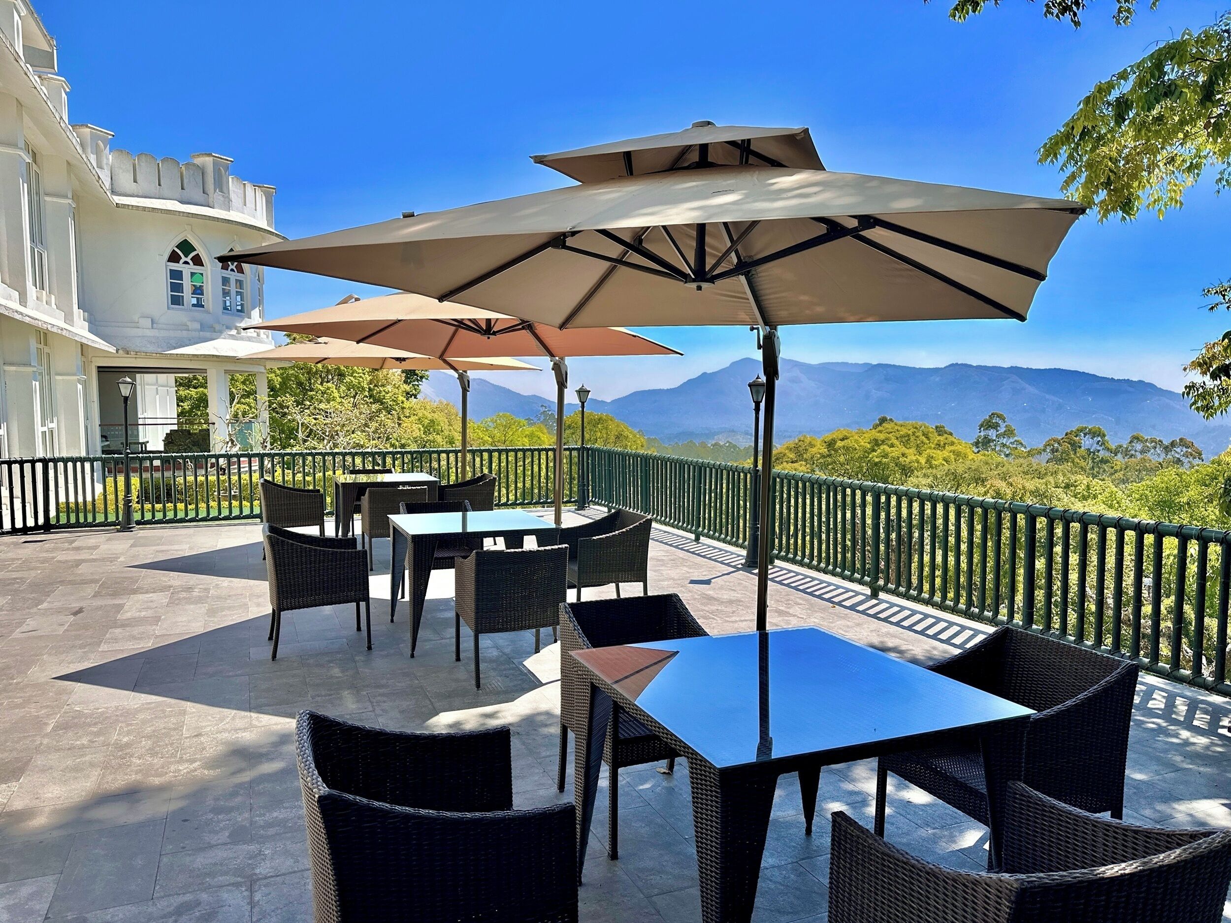 Un patio al aire libre con mesas, sillas, sombrillas y vistas a montañas.