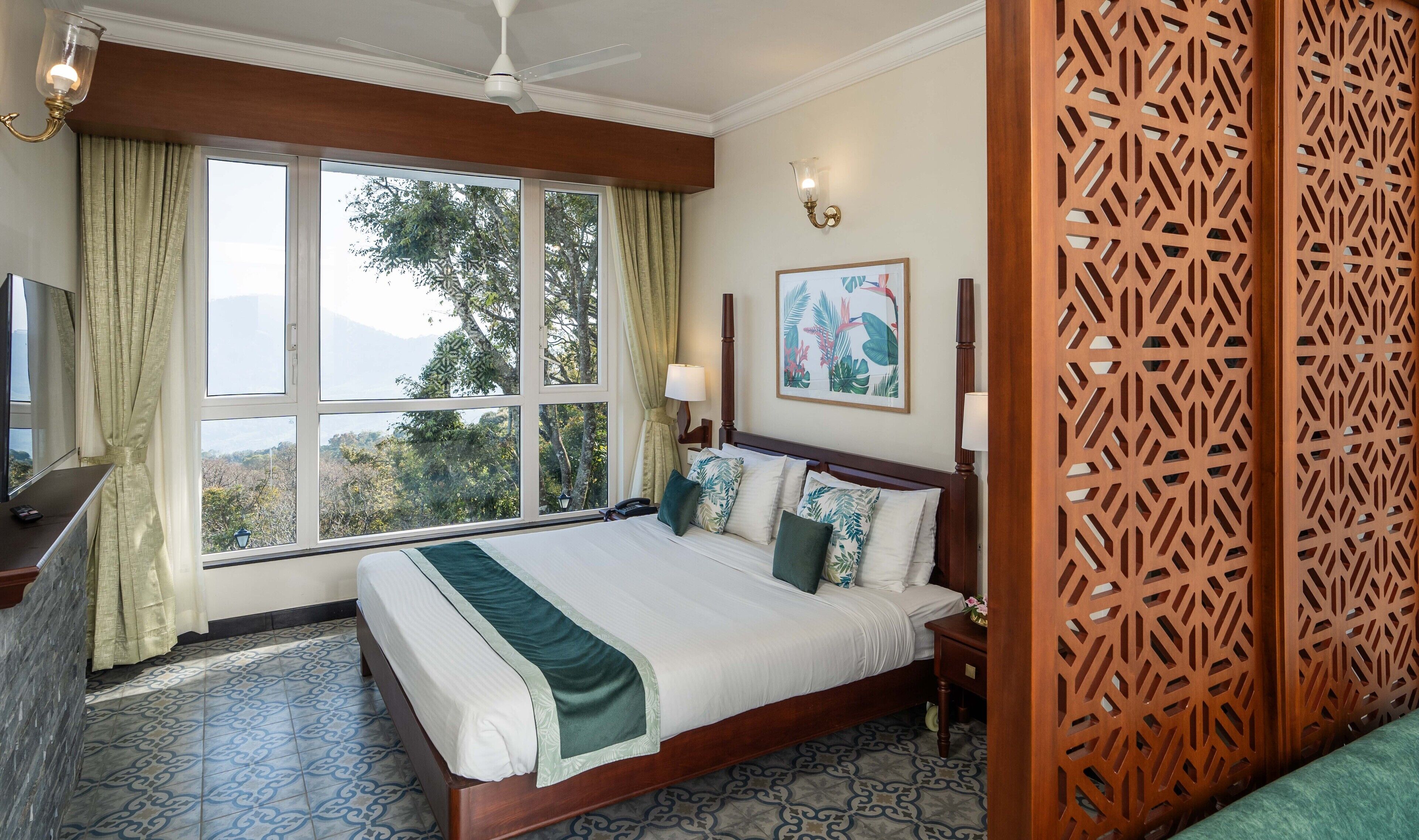Habitación de hotel con una cama grande, televisión, escritorio y ventana con cortinas.