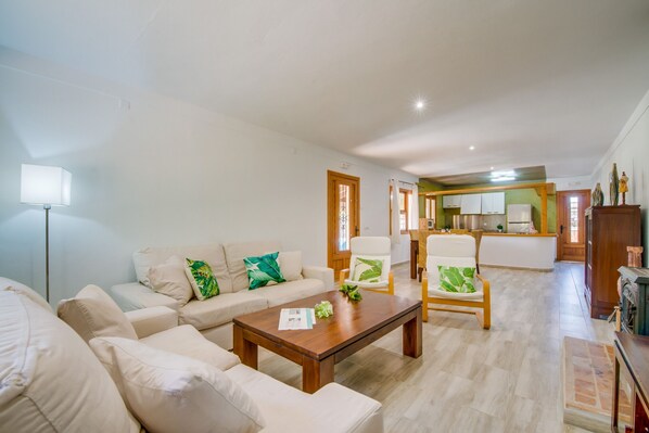 Un salón espacioso con un conjunto de sofás, una mesa de centro y dos sillones. Se observa una cocina al fondo.