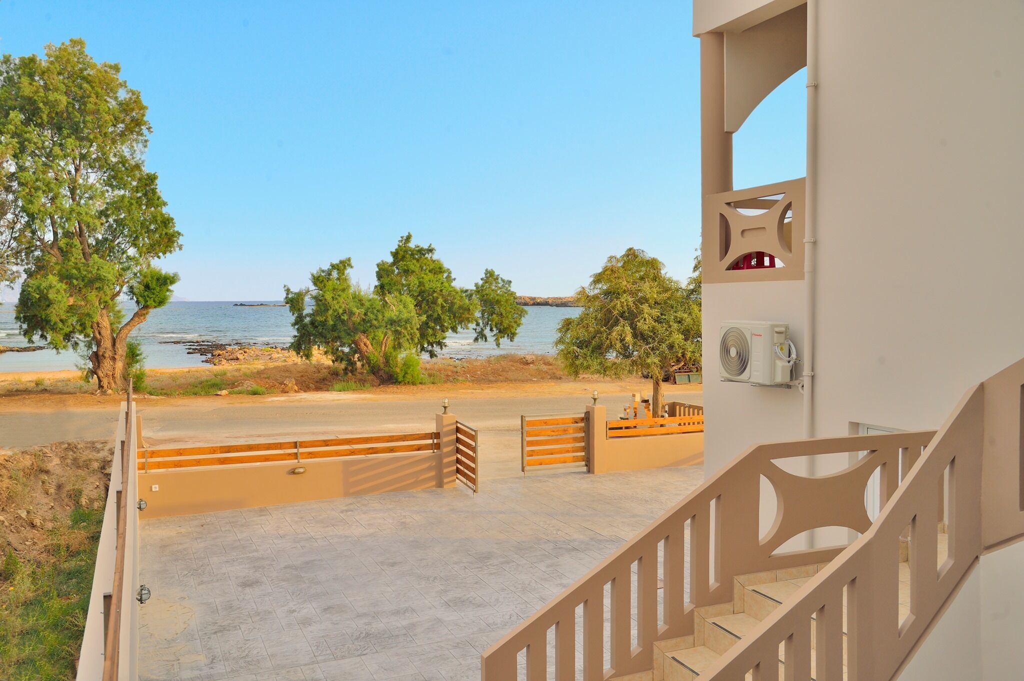 A view from a balcony overlooking a beach with trees and a clear sky.
