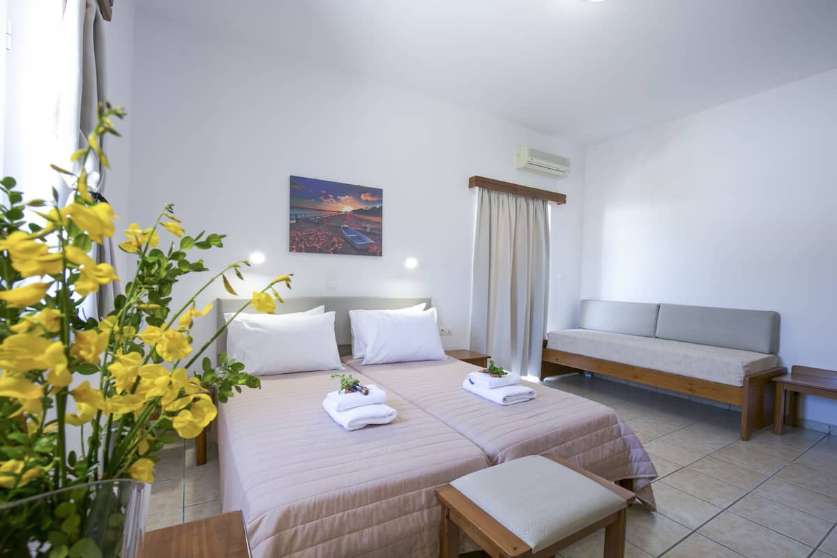 A hotel room with two beds, a sofa, a small table, and a window with curtains.