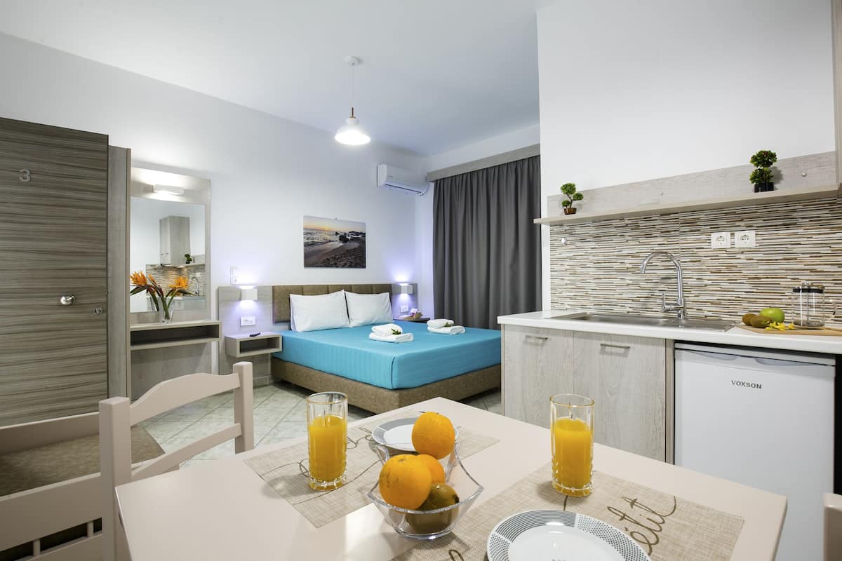 A modern hotel room with a bed, bedside table, and a small kitchenette.