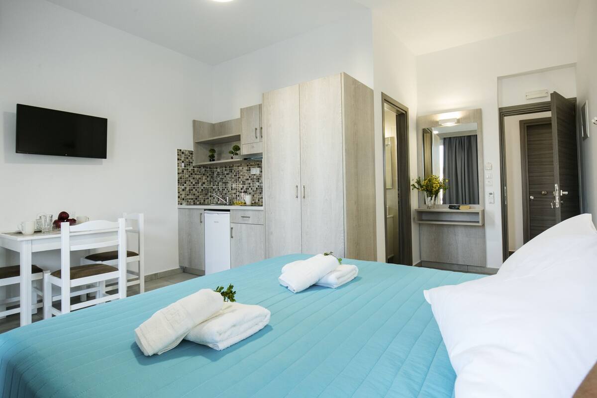 A hotel room with a bed, a desk, a TV, a kitchenette, and a bathroom.