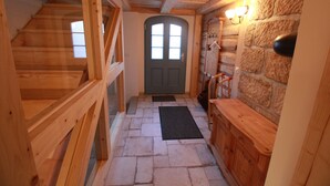 Eine Holztreppe führt zu einer Tür mit einem Fenster, eine Steinsäule mit einem an der Wand befestigten Kleiderhaken und eine hölzerne Bank.