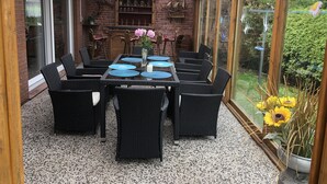 A covered patio with a dining table, chairs, and a hanging light fixture. - Holiday house "Nordsee Pur" (Halbemond)
