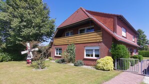 A two-story brick house with a sloped roof, a wooden front porch, and a small garden with a windmill. - Holiday house "Nordsee Pur" (Halbemond)