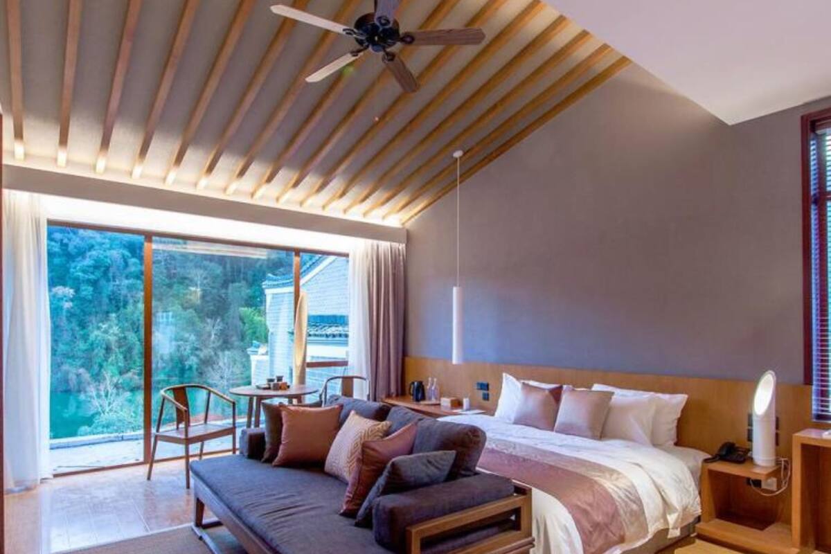 A modern bedroom with a large bed, a bench, a table, and a ceiling fan.