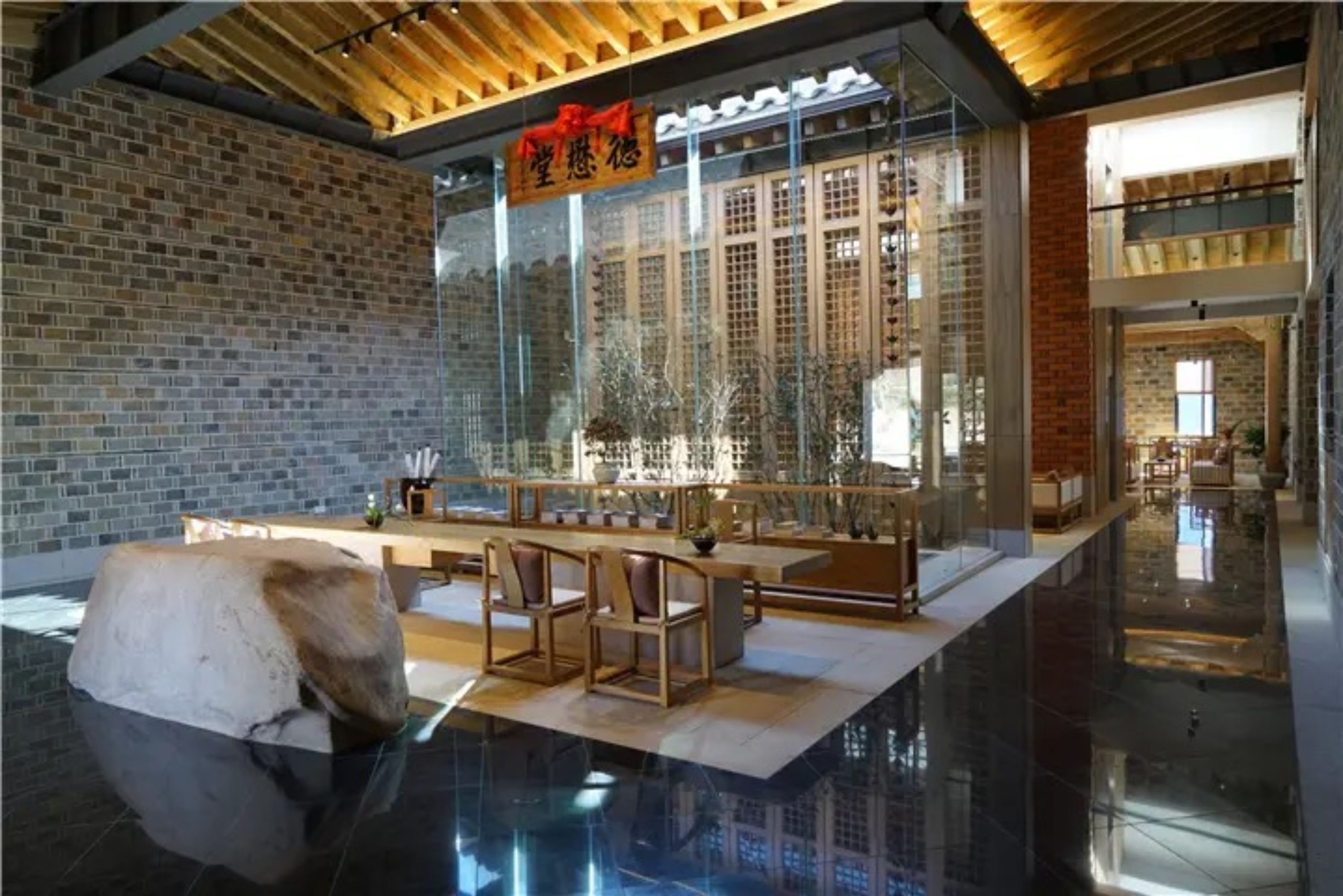 A modern interior with a glass partition, wooden furniture, and a brick wall.