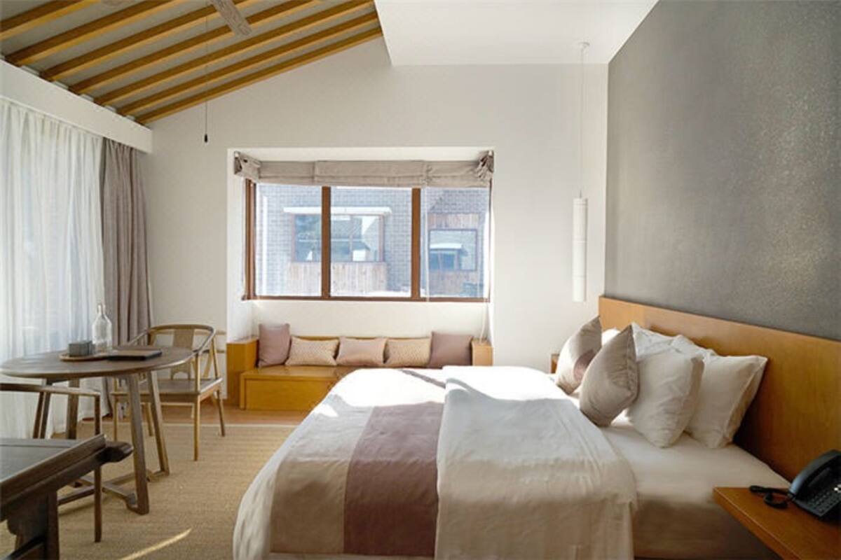 A hotel room with a bed, a desk, a chair, a sofa, and a window with a view of buildings.