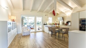 Une cuisine spacieuse avec un plancher en bois, un coin repas avec des chaises, un réfrigérateur blanc et une grande fenêtre donnant sur un paysage verdoyant.