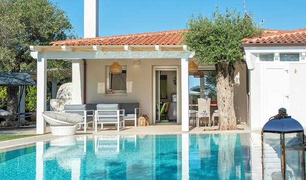 A pool area with a pergola, lounge chairs, and a covered seating area.