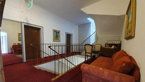 En trappe med gelænder fører op til en platform. Der er et rødt tæppe med sofa og stole.