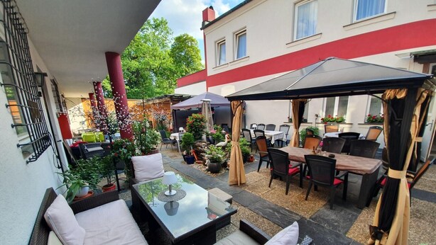 En udendørs patio med fletmøbler, et glasbord og en overdækket siddeplads.