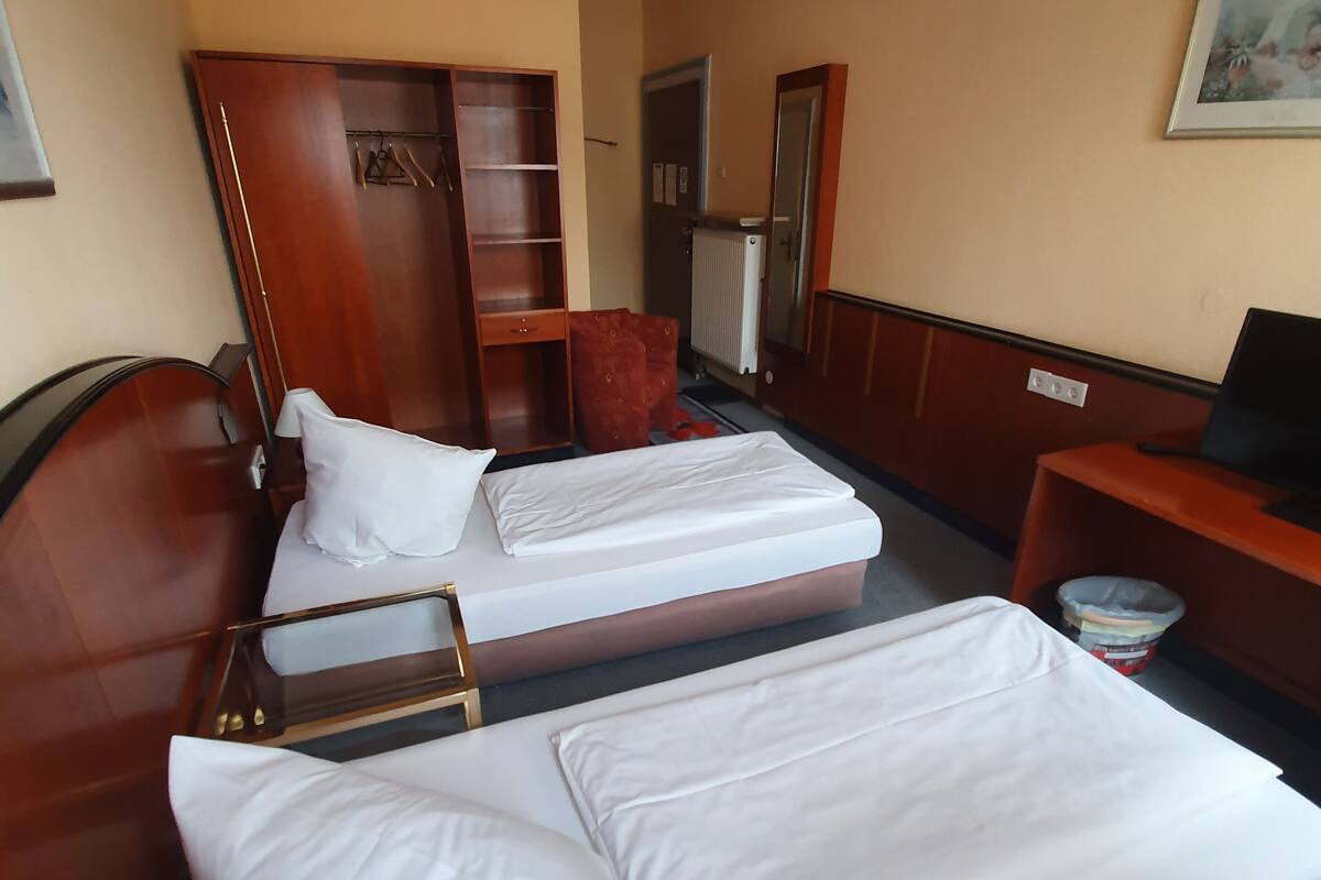 A hotel room with two single beds, a wooden wardrobe, a desk with a chair, and a radiator.