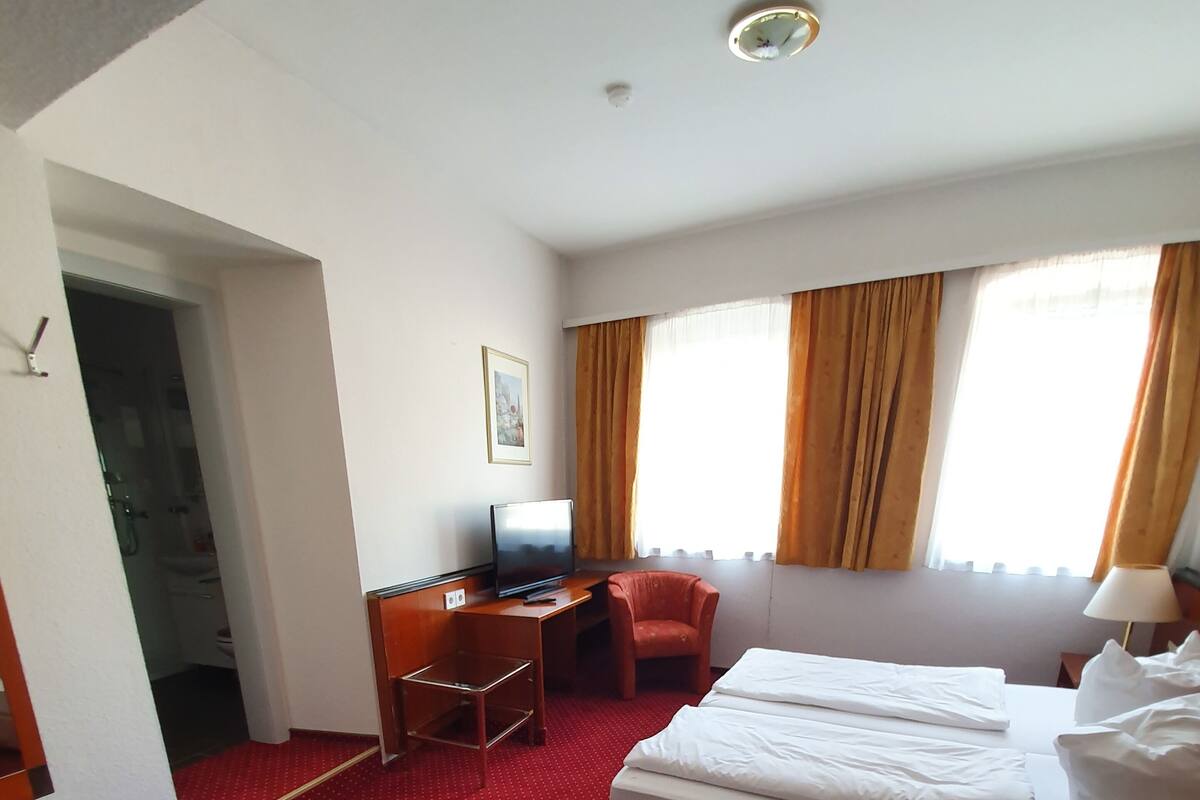 A hotel room with a bed, a desk, a chair, and a television.