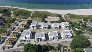 Una vista aerea di una zona residenziale costiera con moderni edifici per appartamenti, una spiaggia e un molo.