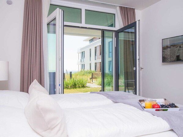 A hotel room with a bed, a breakfast tray, and a view of a building and greenery outside.