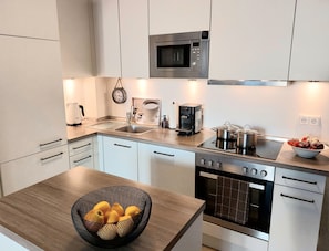 A modern kitchen with white cabinets, a stainless steel microwave, a coffee maker, and a bowl of fruit on the counter.