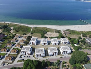 An aerial view of a coastal residential area with modern apartment buildings, a beach, and a pier.