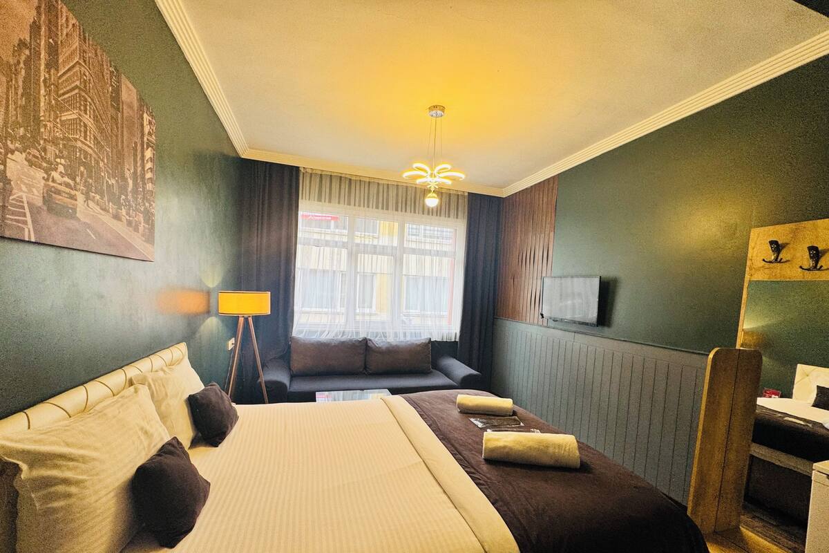 A hotel room with a bed, a sofa, a TV, and a window with curtains.