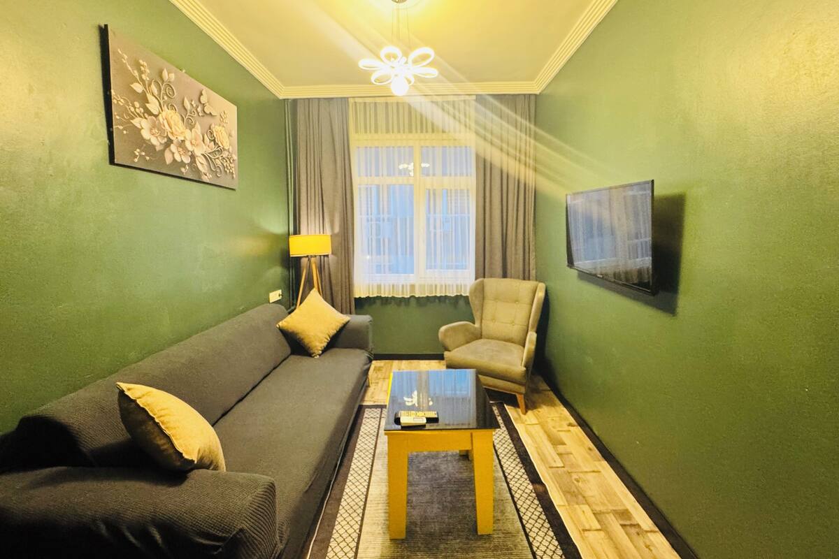 A living room with a sofa, armchair, coffee table, and a TV on the wall.