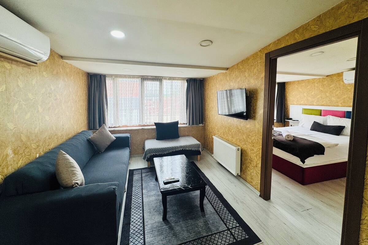 A hotel room with a sofa, a small table, a TV, and a bed with colorful pillows.