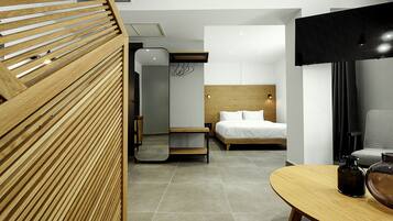 A modern hotel room with a wooden slatted partition, a bed with white linens, a bedside table, a mirror, and a flat-screen TV mounted on the wall.