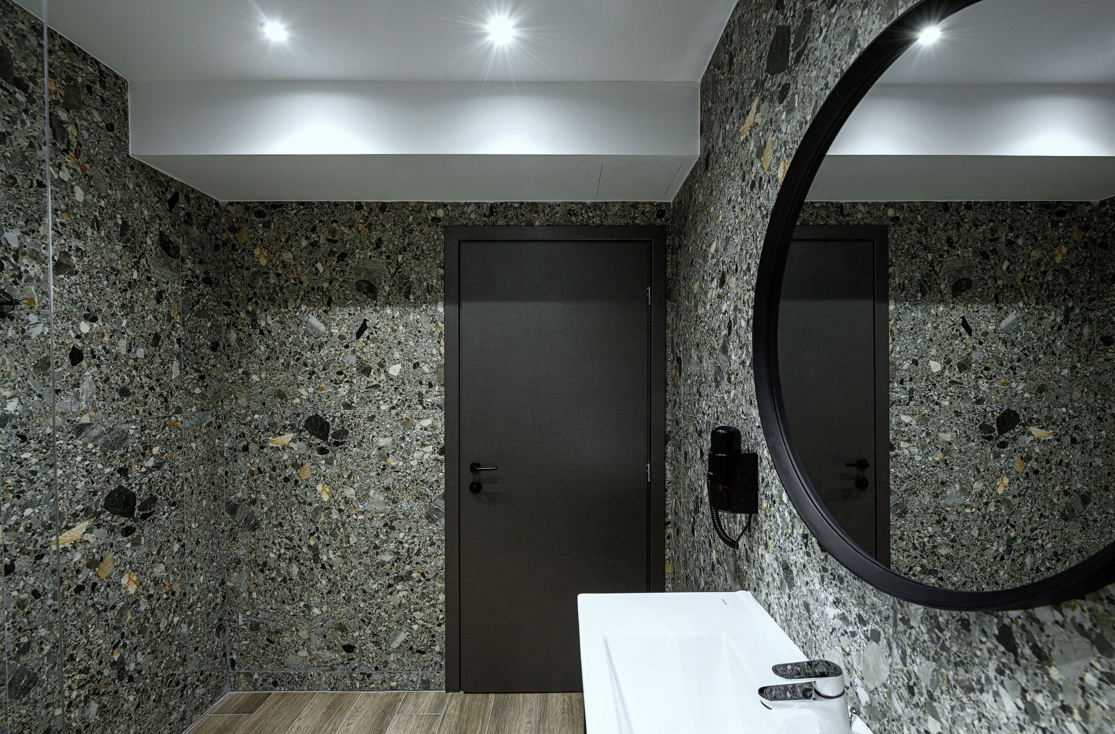 Une salle de bain avec un mur en granit, un lavabo blanc et une porte dotée d’une serrure à clé.