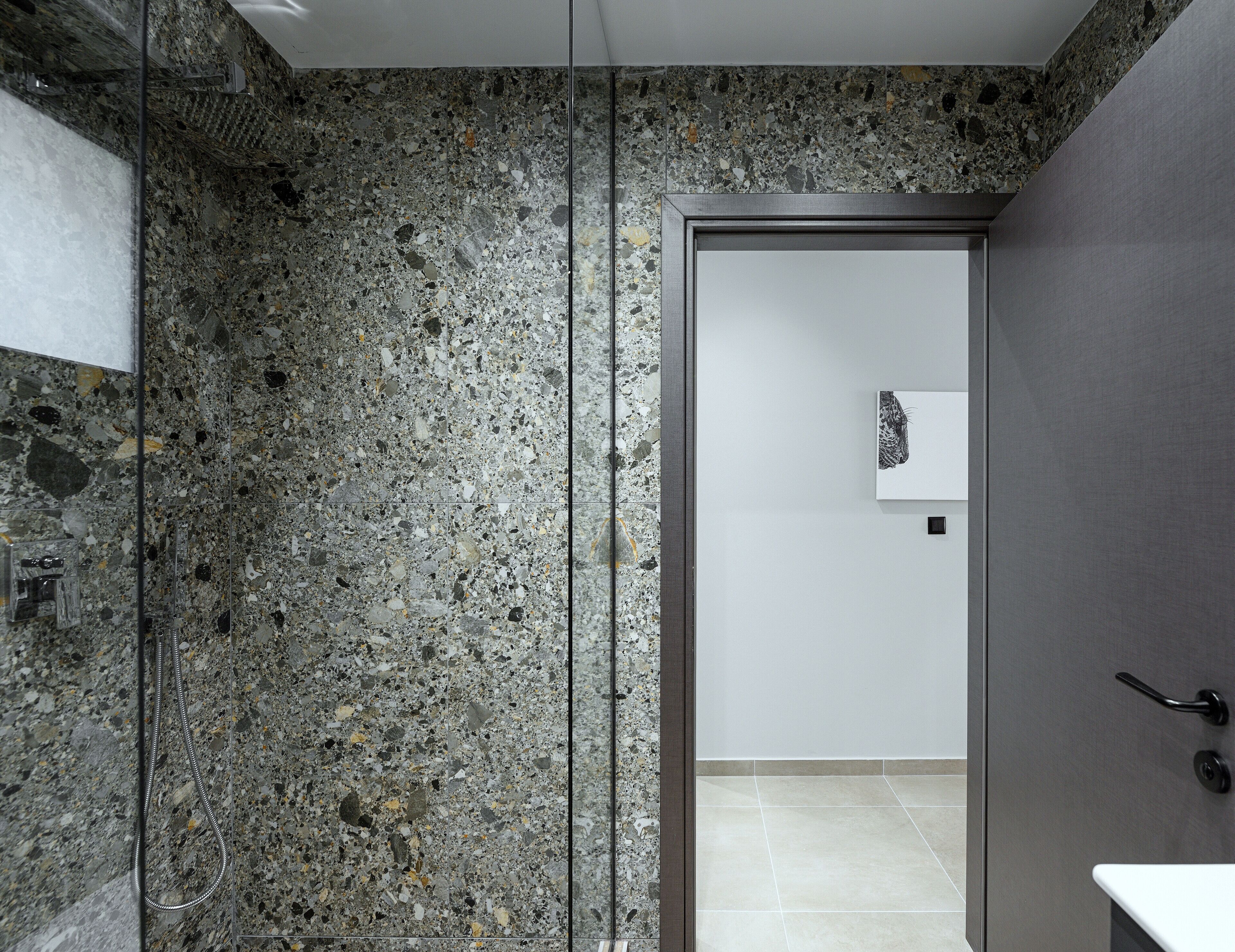 A modern bathroom with a speckled granite floor, a glass shower enclosure, and a minimalist design.