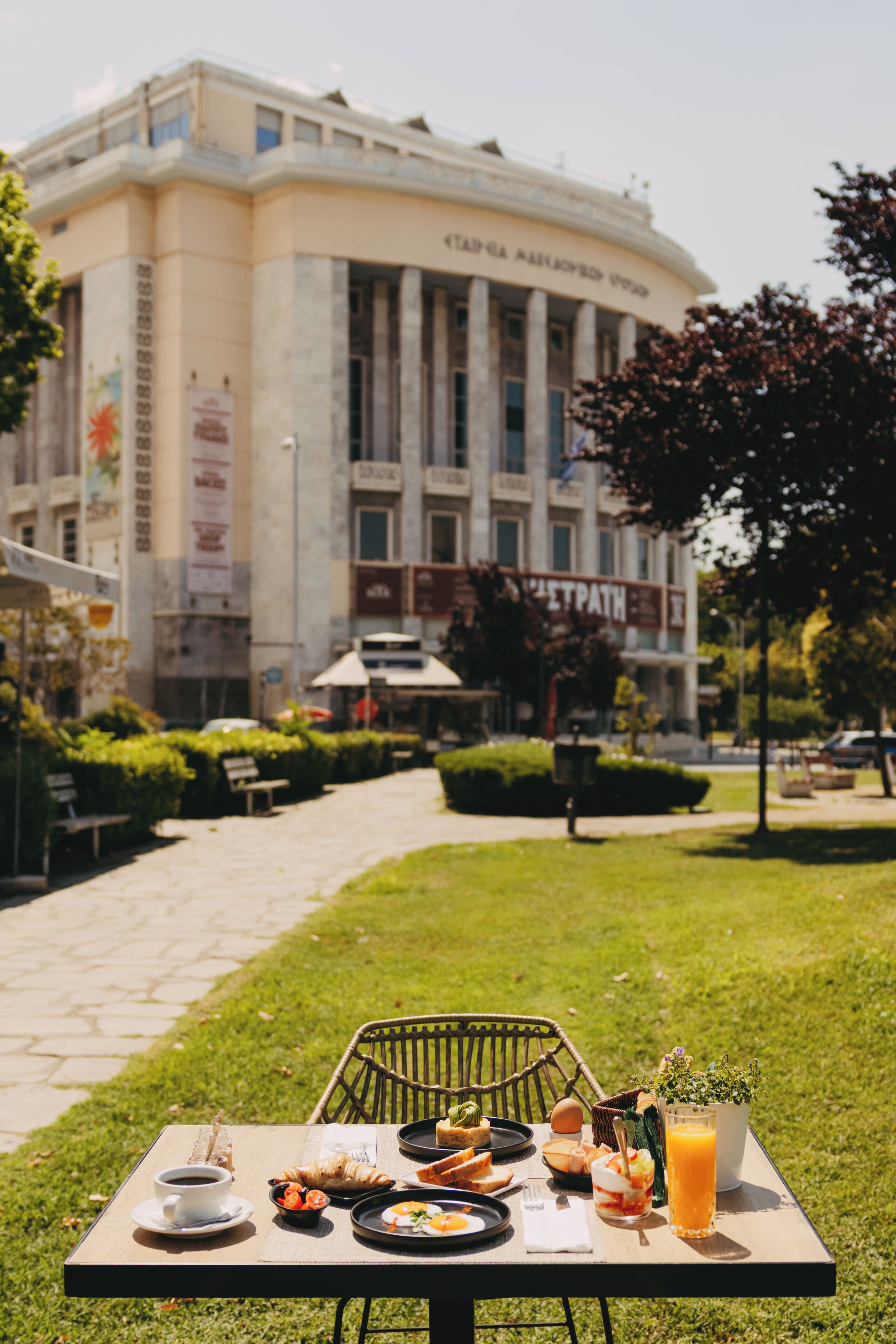 An outdoor dining table with food and drinks, a bench, and a building with columns in the background.