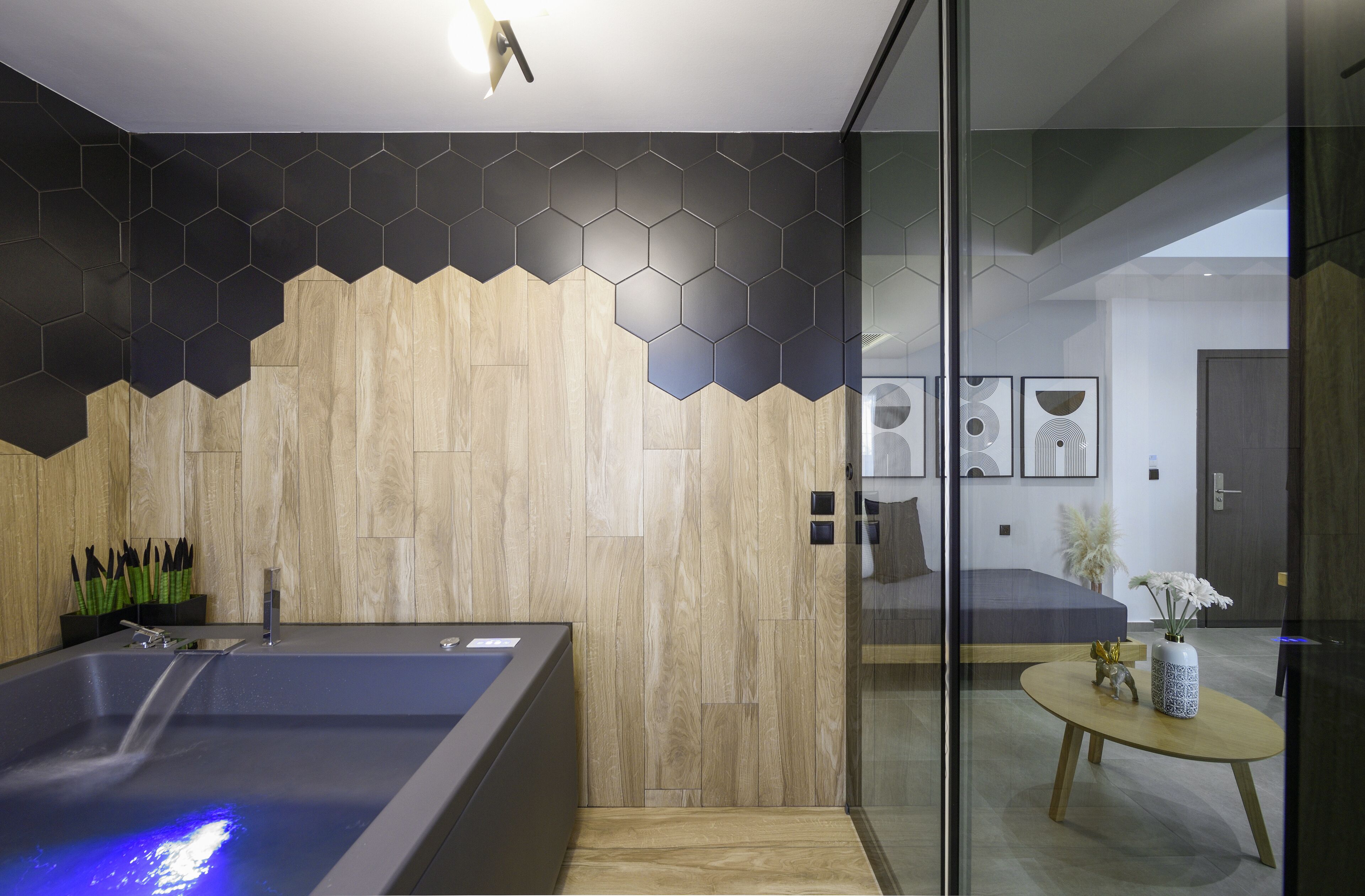 Un baño moderno con pared de madera, mampara de ducha de vidrio y bañera con luz azul.